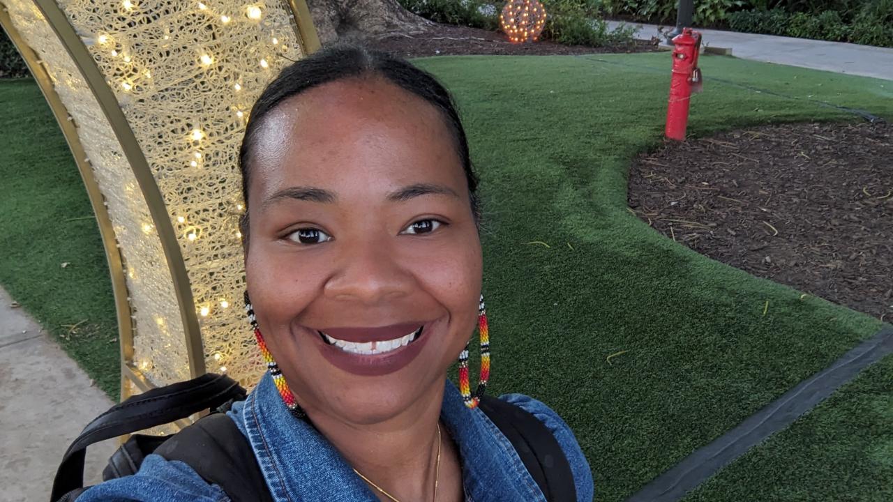 Dawniell Black smiles in front of a grassy lawn and a light structure. She is wearing hoop earrings and a denim jacket.