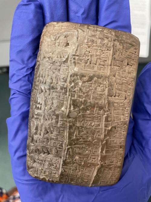Small Mesopotamean tablet, brown in color with text, held in a blue-gloved hand