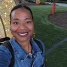 Dawniell Black smiles in front of a grassy lawn and a light structure. She is wearing hoop earrings and a denim jacket.